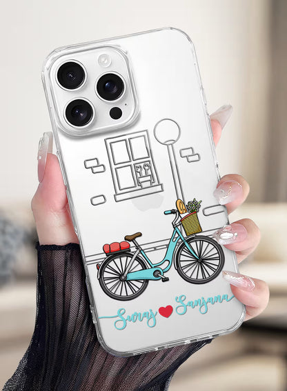 Custom couple names Suraj and Sanjana printed in teal script with a red heart on a clear silicone phone case featuring a vintage bicycle illustration.