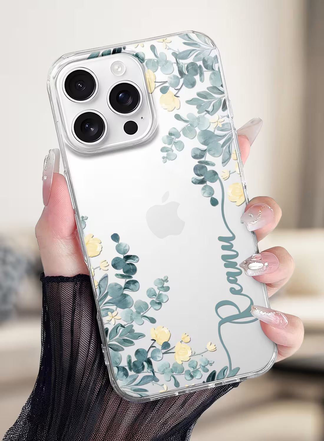 Custom name Reanu printed vertically in teal script on a clear silicone phone case featuring a watercolor eucalyptus and yellow floral design.