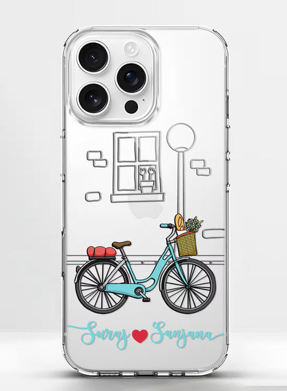 Custom couple names Suraj and Sanjana printed in teal script with a red heart on a clear silicone phone case featuring a vintage bicycle illustration.